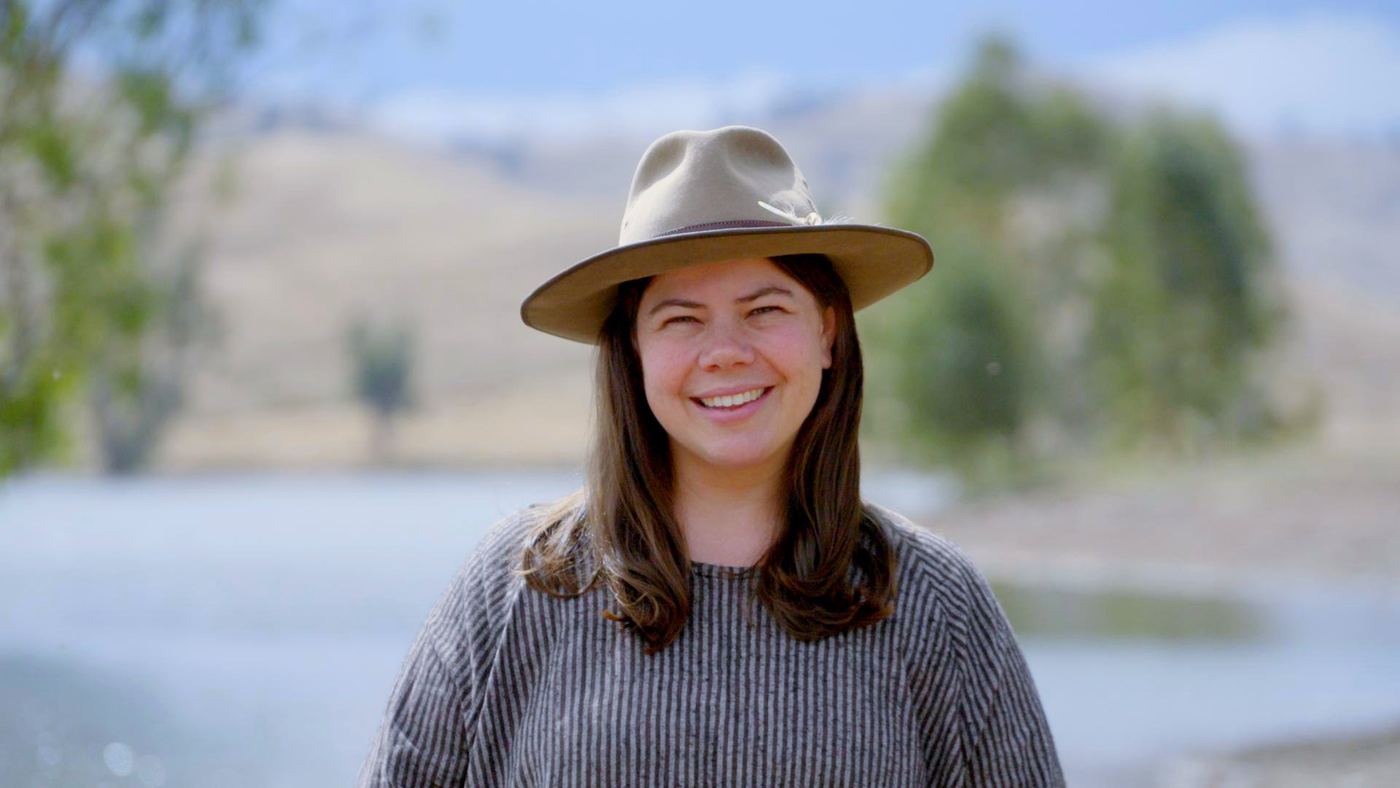 A smiling woman in a wide-brimmed hat by a lake