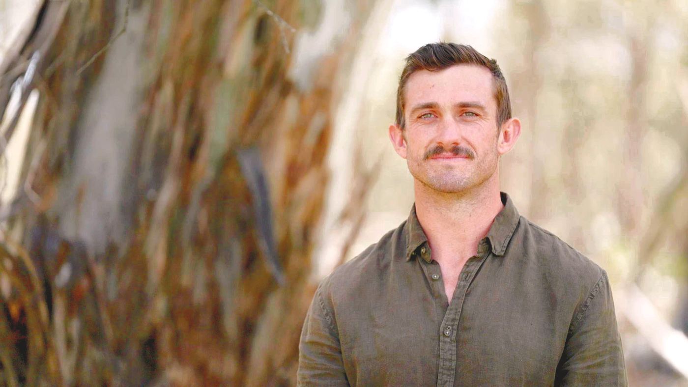 A man with a moustache in front of eucalyptus bark