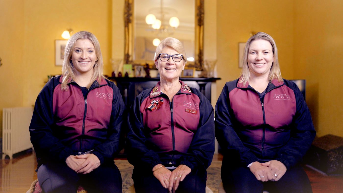 Three women in matching jackets seated in an ornate room