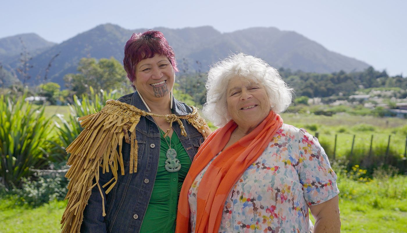 Two women laughing in front of green hills