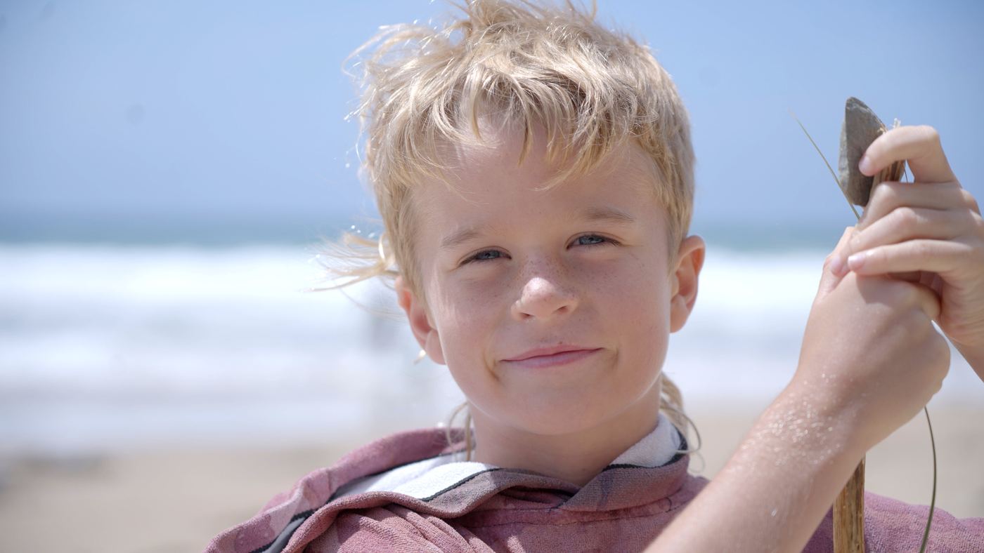 A boy on a beach holding up a find